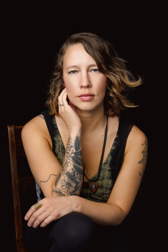 Woman with tattoos and brown hair with green tank top poses for headshot