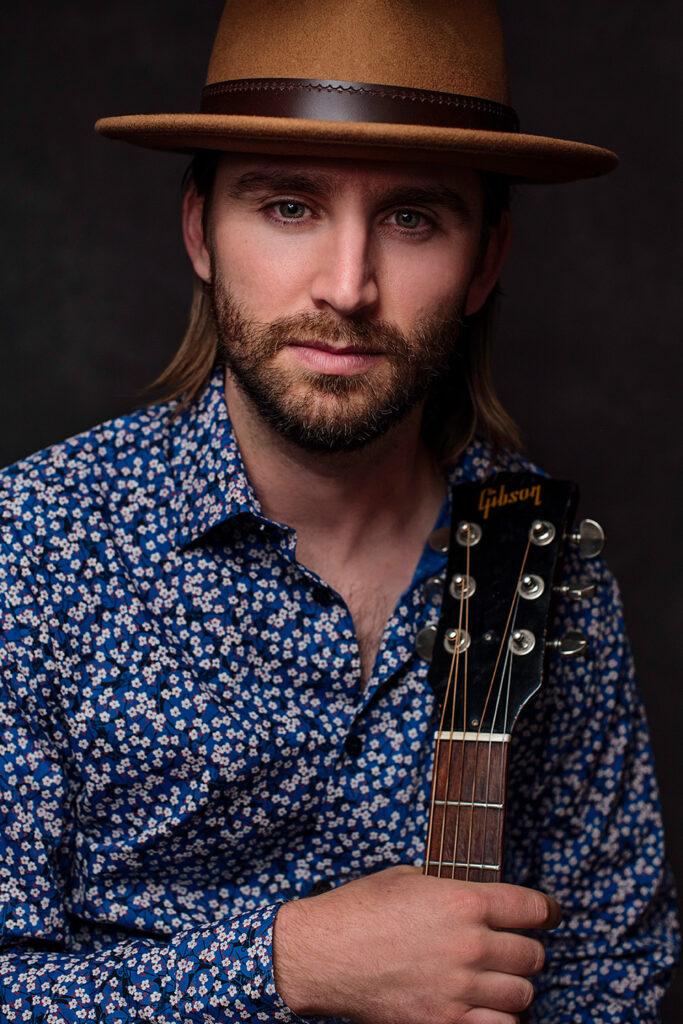 Andrew Camp looks into the camera holding a guitar