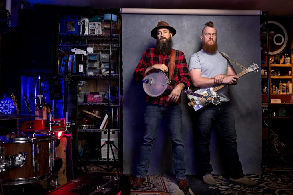 Band Duo in pose in garage with banjo and cigar box guitar