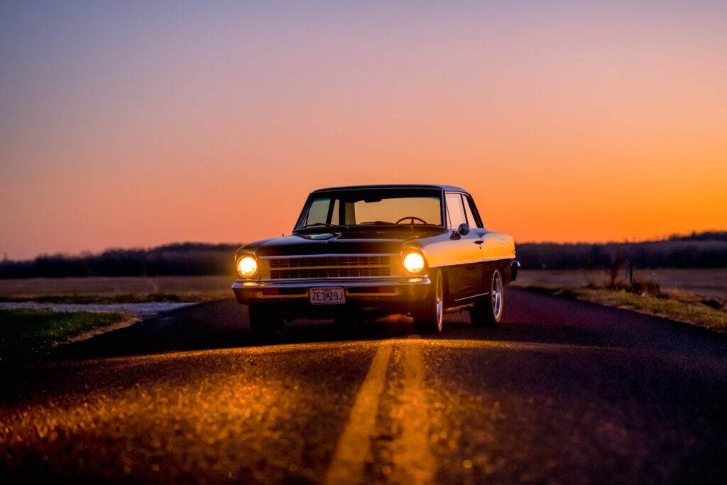 Side profile of vintage refurbished Chevy II at night with headlights on