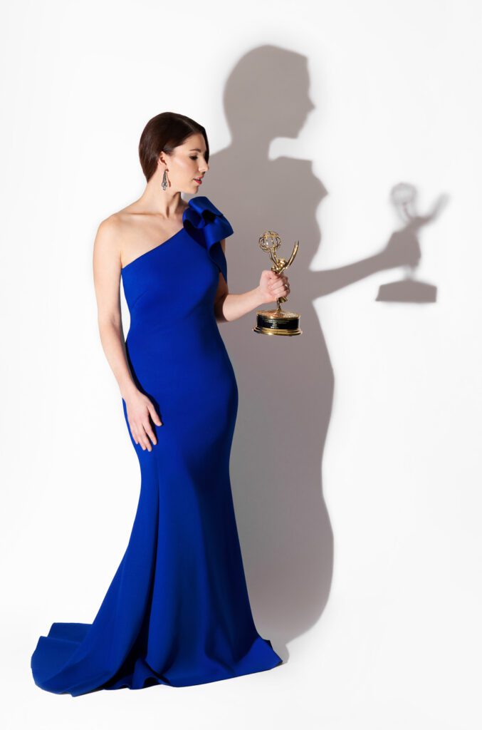 Model wearing blue evening gown holding Emmy statue.