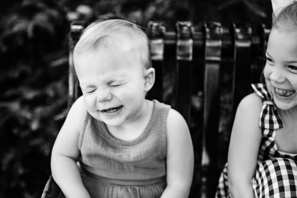 Sister laughs at youngest sister as she smiles and closes her eyes.
