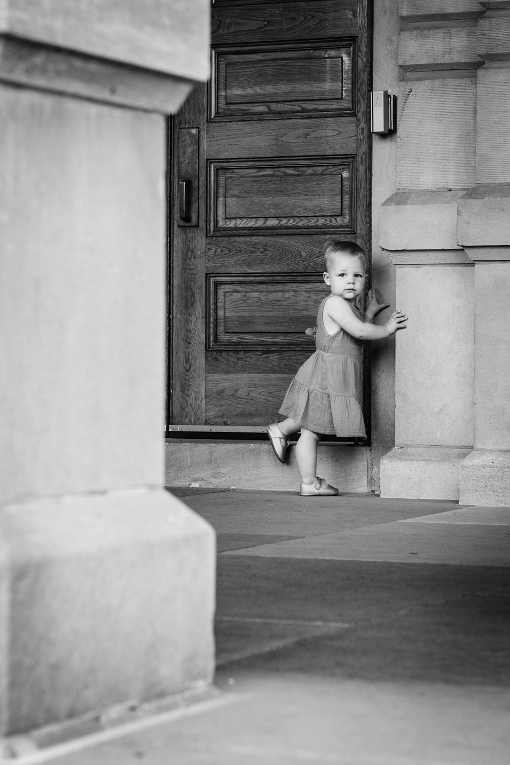 Toddler leans onto large wooden door.