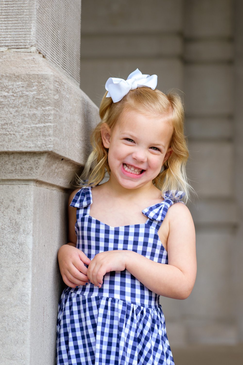 A cute smile on young child wearing blue and white dress with bows.