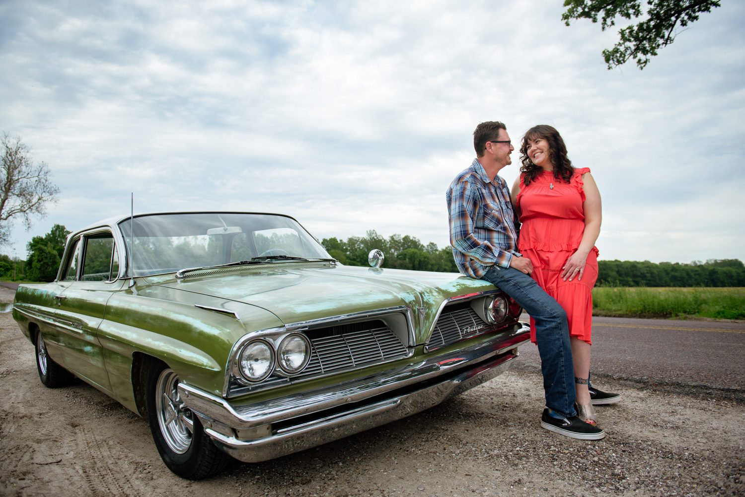 Couple smile at each other sitting on vintage Pontiac car