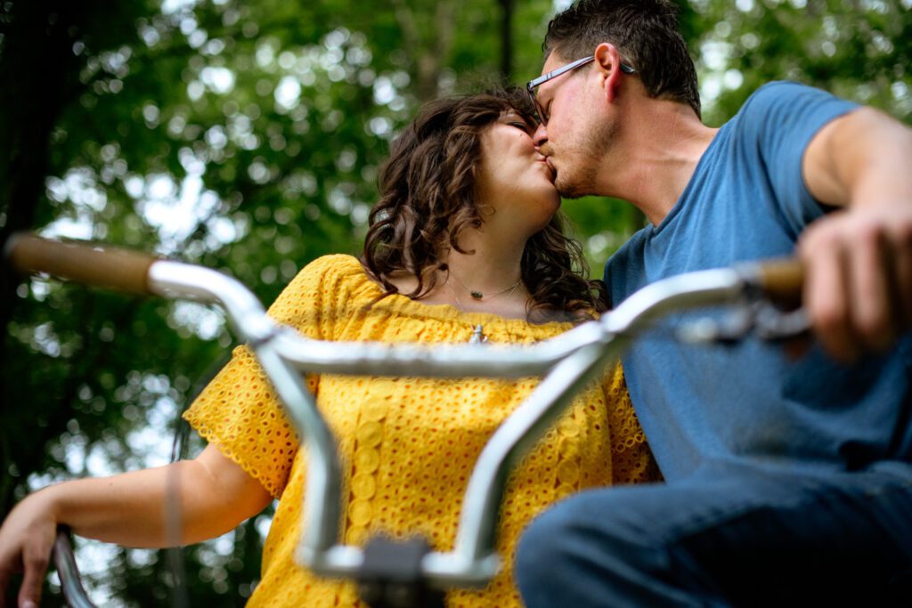 Couple wearing yellow and blue kiss while sitting on bikes.
