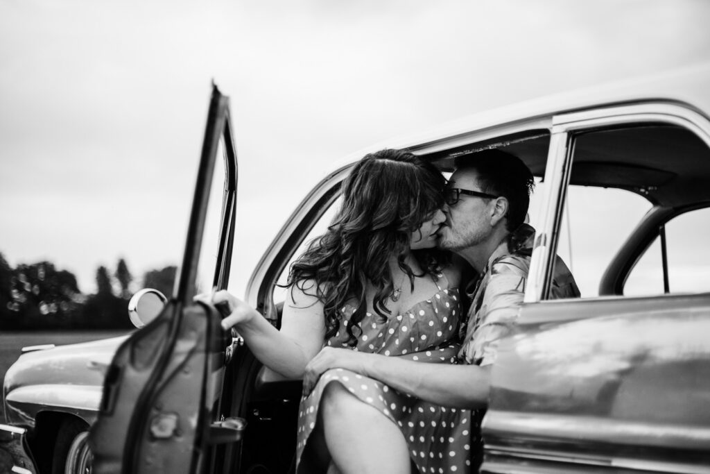 Engaged couple kiss while sitting in Pontiac Catalina with door open.