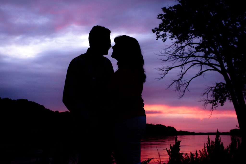 Silhouette of couple next to river at sunset.