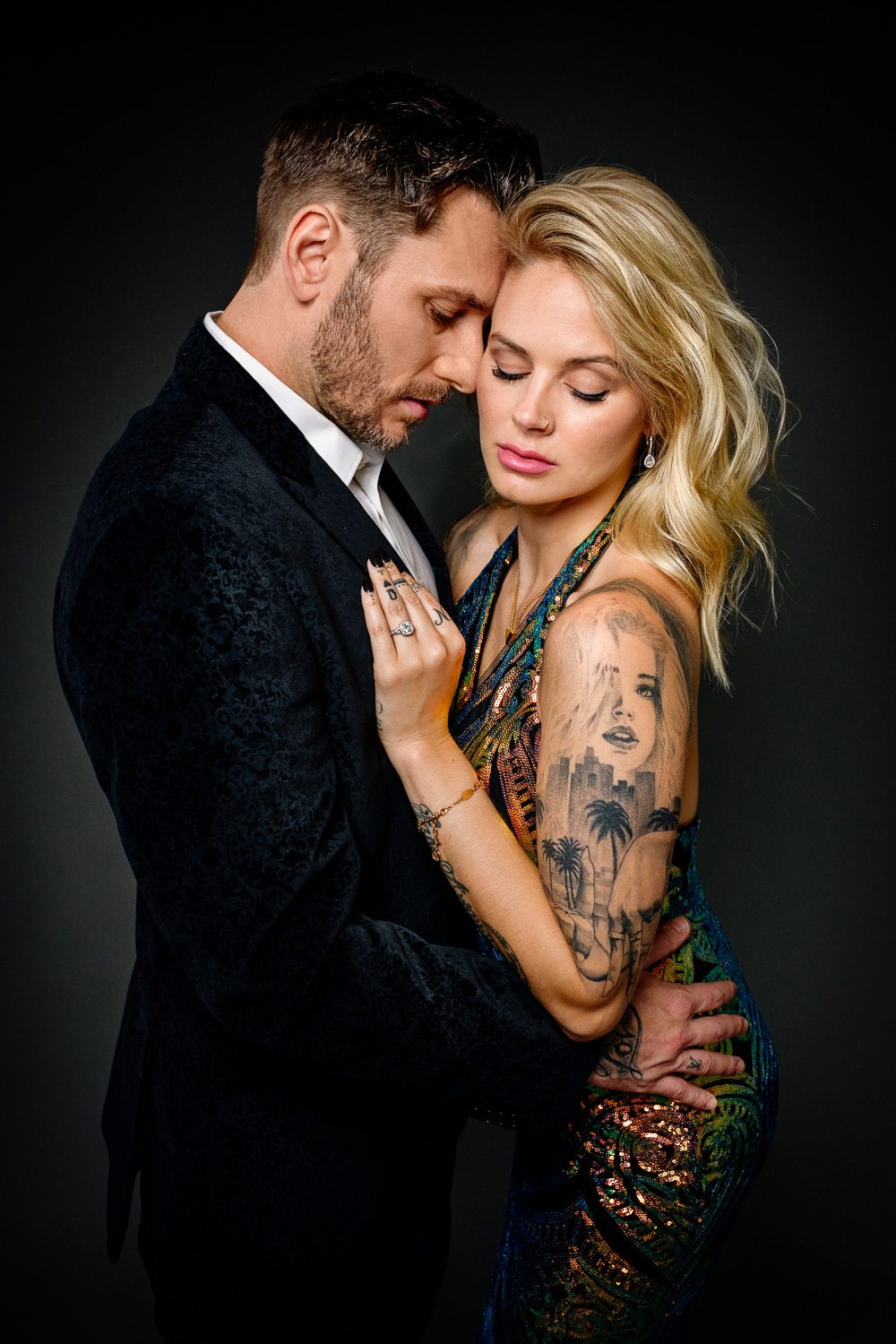 Romantic couple wearing velvet jacket and colorful sequin evening gown cuddle together.