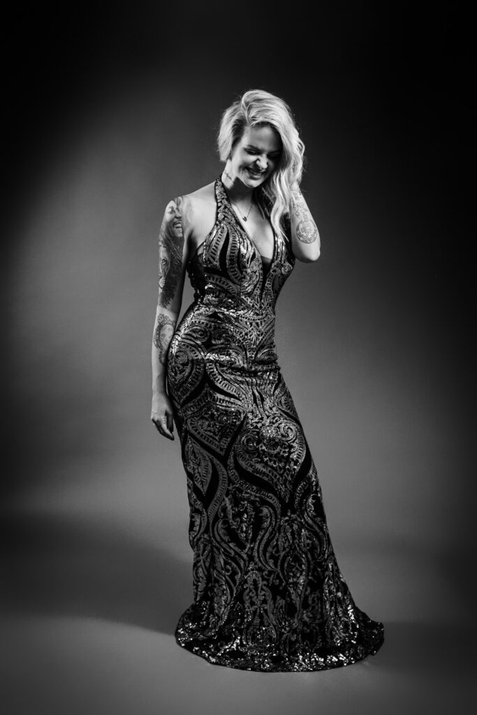 blonde woman laughs as she looks down while posing in a sequin evening gown.