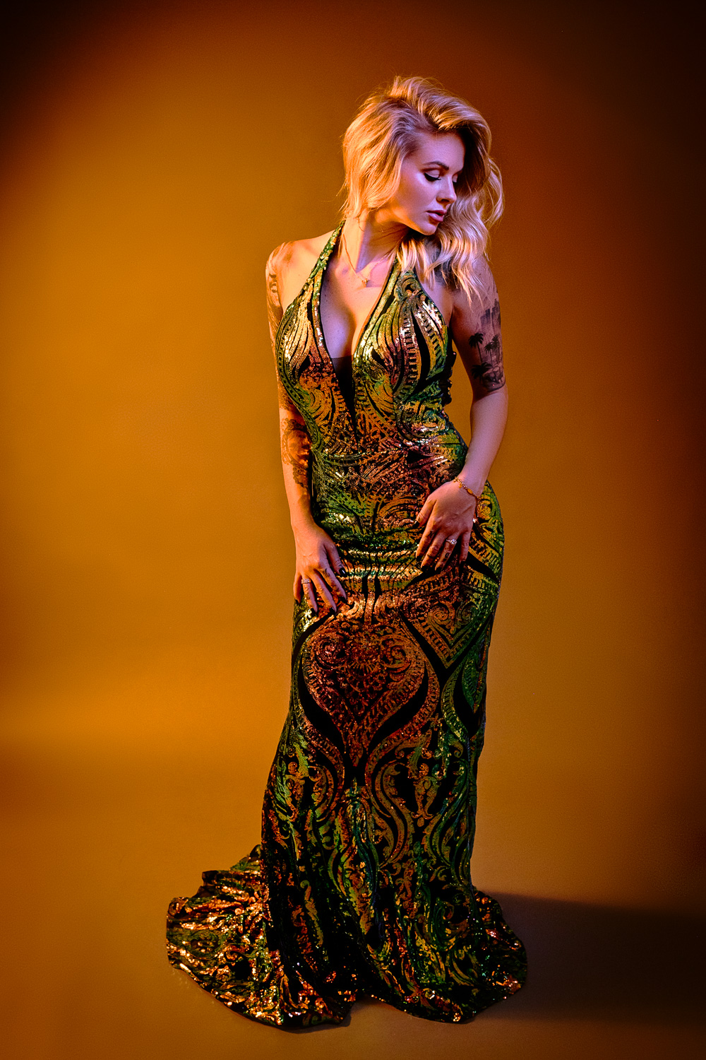 Beautiful blonde woman wearing an orange and green sequin evening gown on an orange backdrop