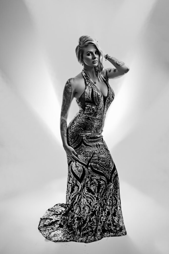 blonde woman wearing a sequin evening gown poses in front of a white and gray graphic background