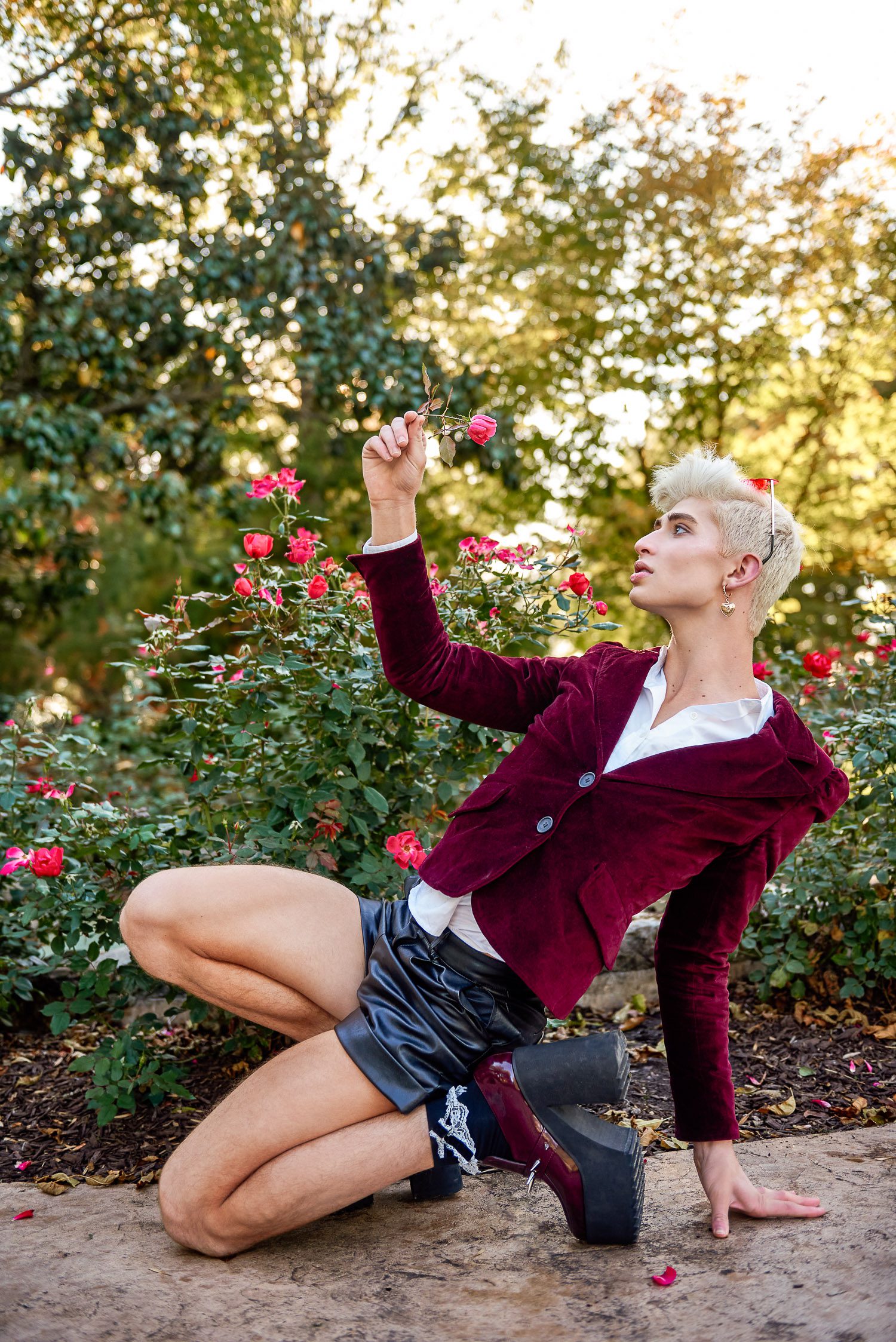 Senior guy wearing red jacket, black shorts and tall boots holds a rose