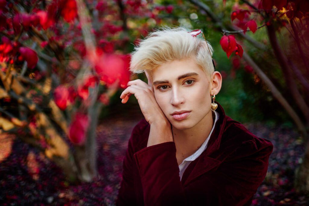 senior zachary willmore poses in front of red leaves wearing red jacket