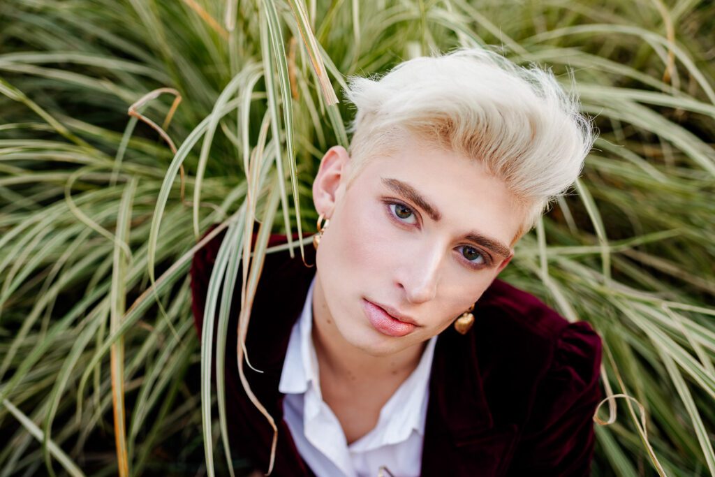 Senior guy wearing burgundy velvet jacket sitting in tall grass.