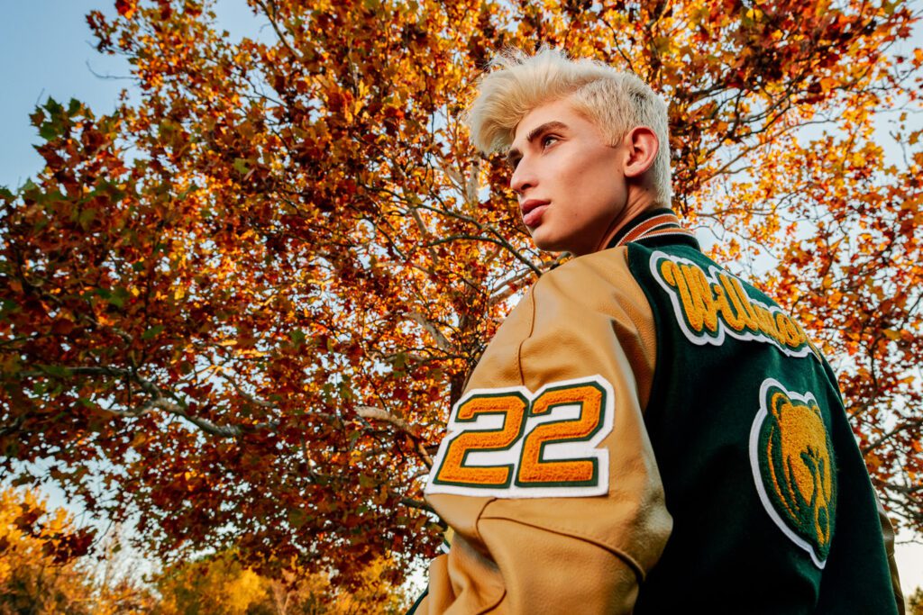 Senior guy wearing green and orange letter man jacket in front of fall colors