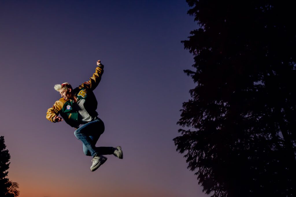 Senior guy cheerleader jumping in front of sunset
