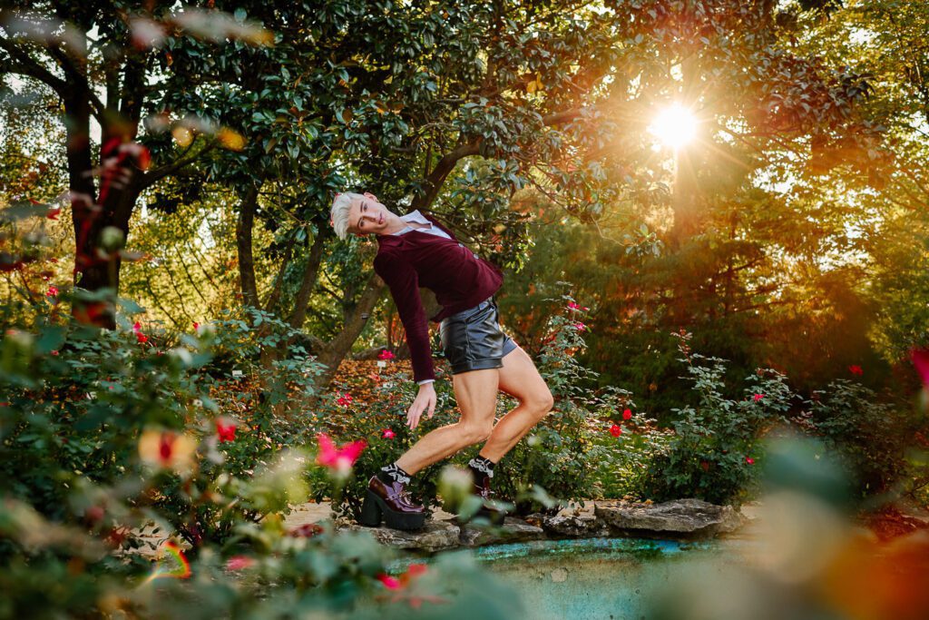 Senior wearing velvet jacket and black leather shorts in flower garden with sunshine coming through trees at Shelter Gardens Columbia Missouri
