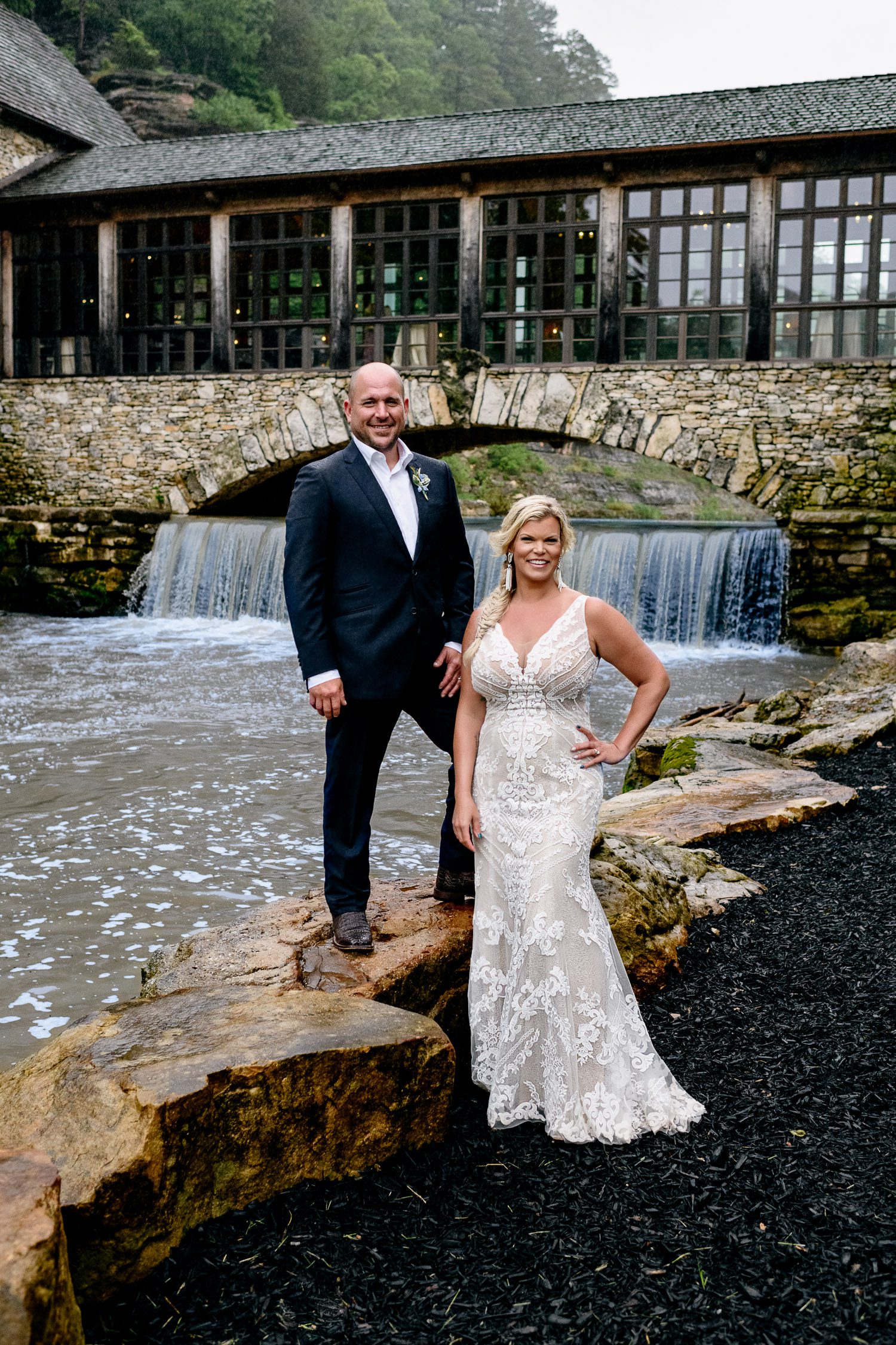 portrait of bride laughing as groom stands on rock in front of Dogwood Canyon Lodge and Grist Mill Lampe Mo Schaefer Photography