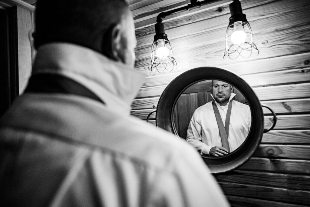 groom starts putting on tie in mirror