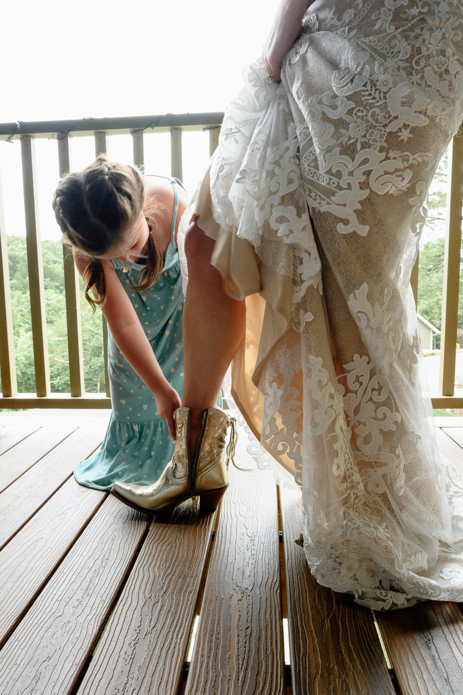 girl wearing blue heart dress helps bride put on gold boots
