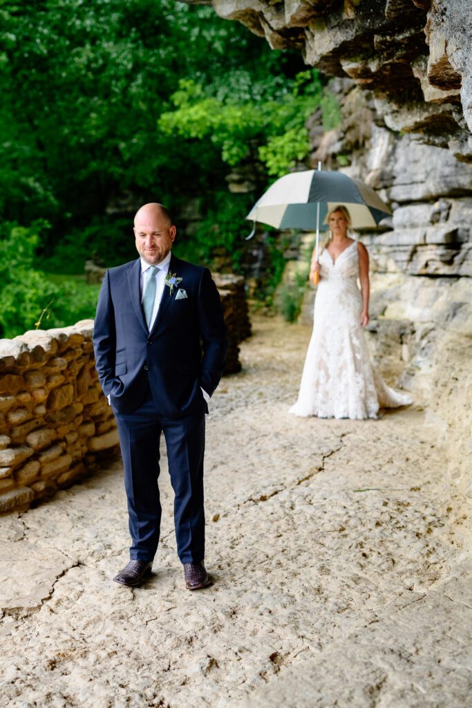 groom standing near great spirit falls waits as bride walks up for first look