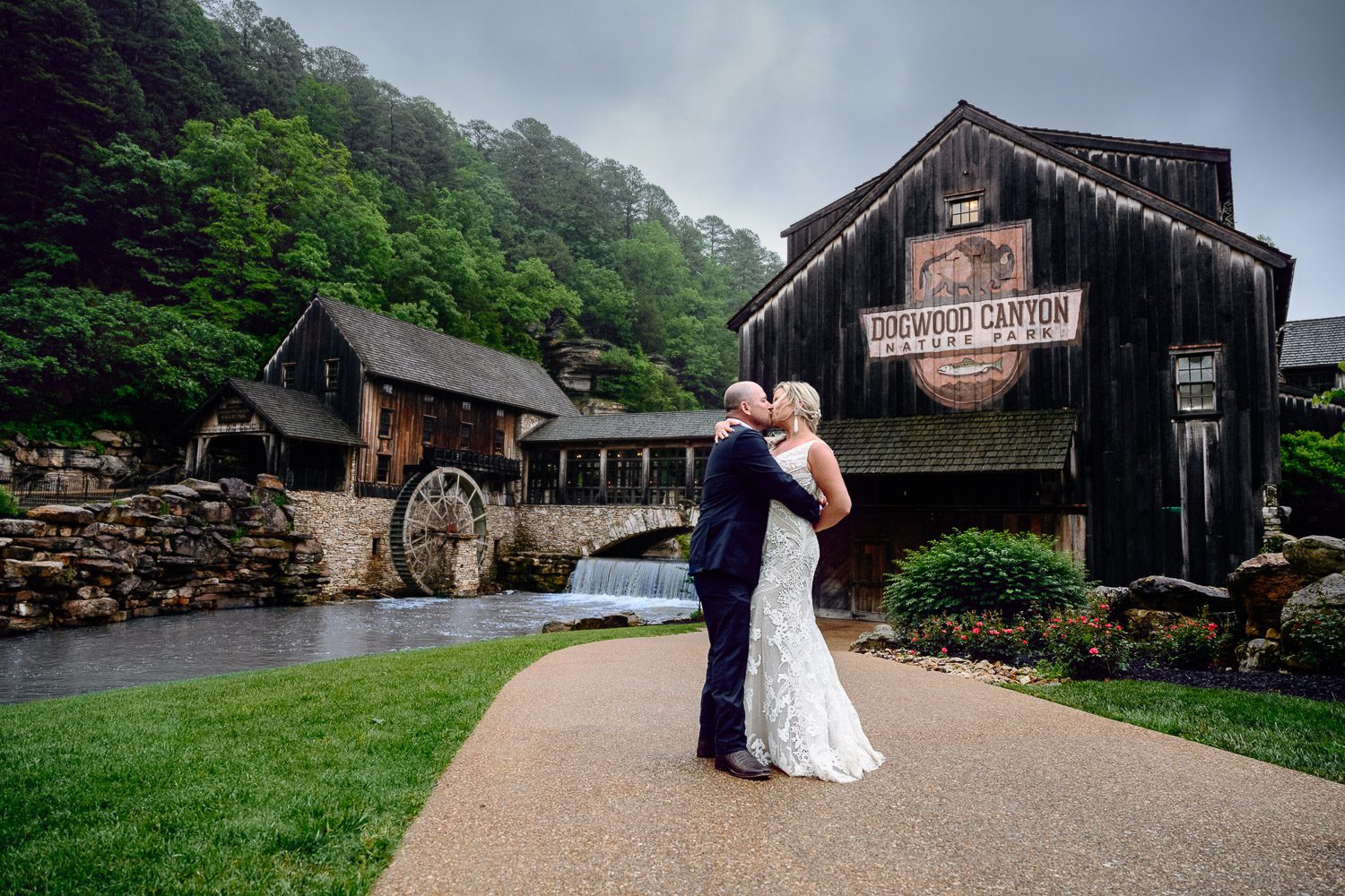 Dogwood Canyon Lodge and Mill behind newlywed Bride and Groom kissing