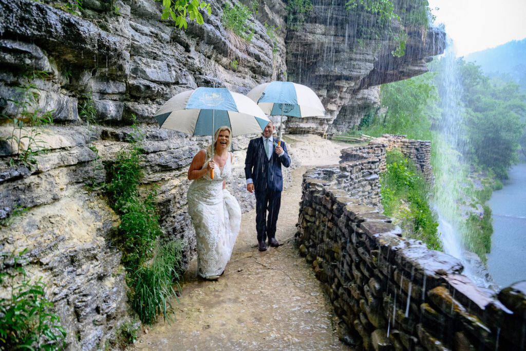 bride and groom walk away with umbrellas in rain at Great Spirit Fall in Dogwood Canyon