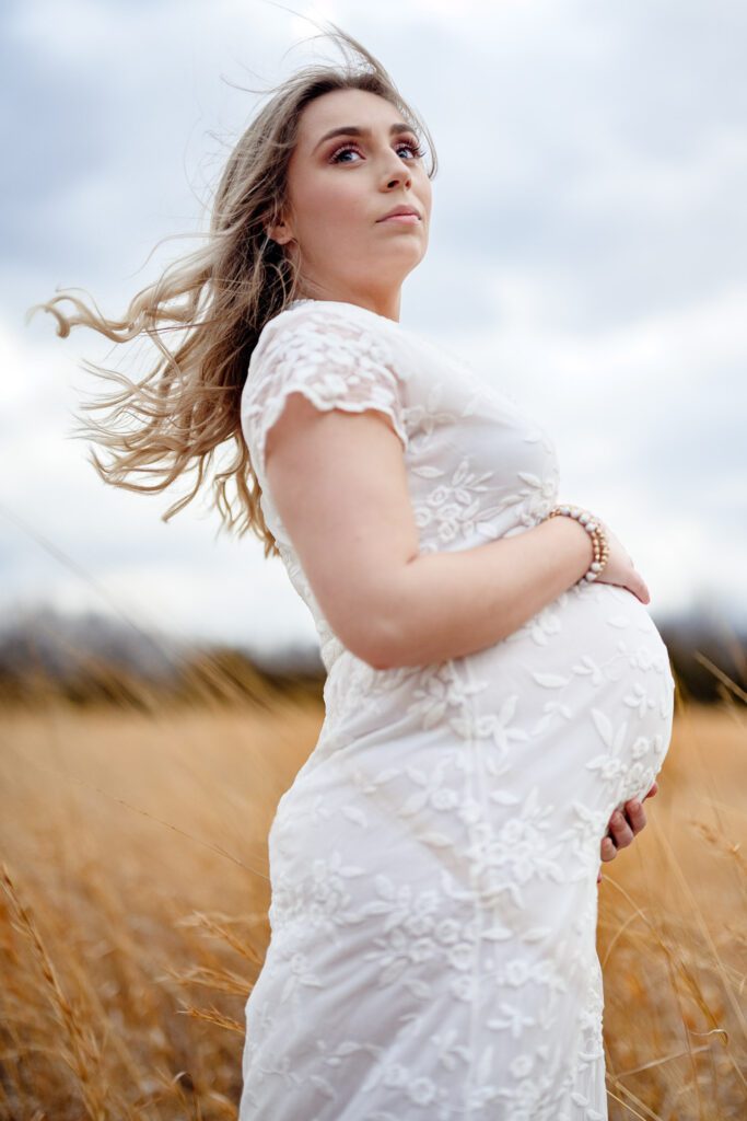 Pregnant maternity photo with mother holding her baby bump with hair blowing in wind.