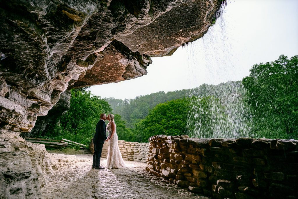 Bride and groom kiss under water fall at Dogwood Canyon.