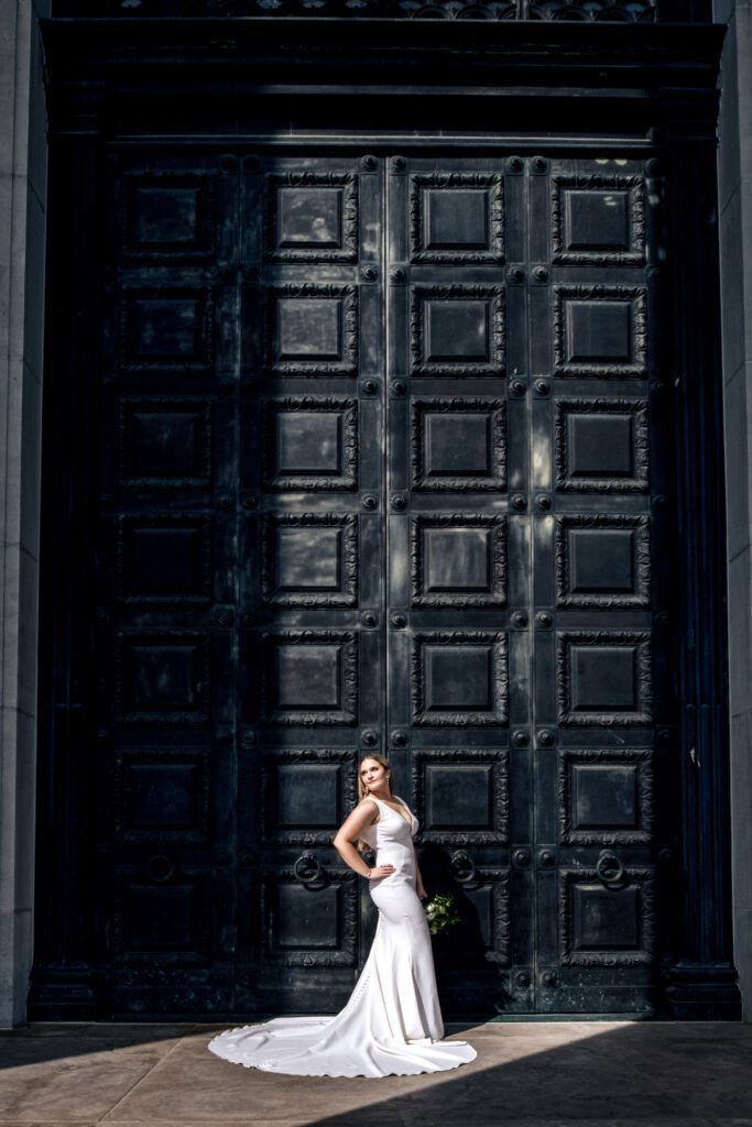 Bride poses in front of large black doors as the sun highlights her.