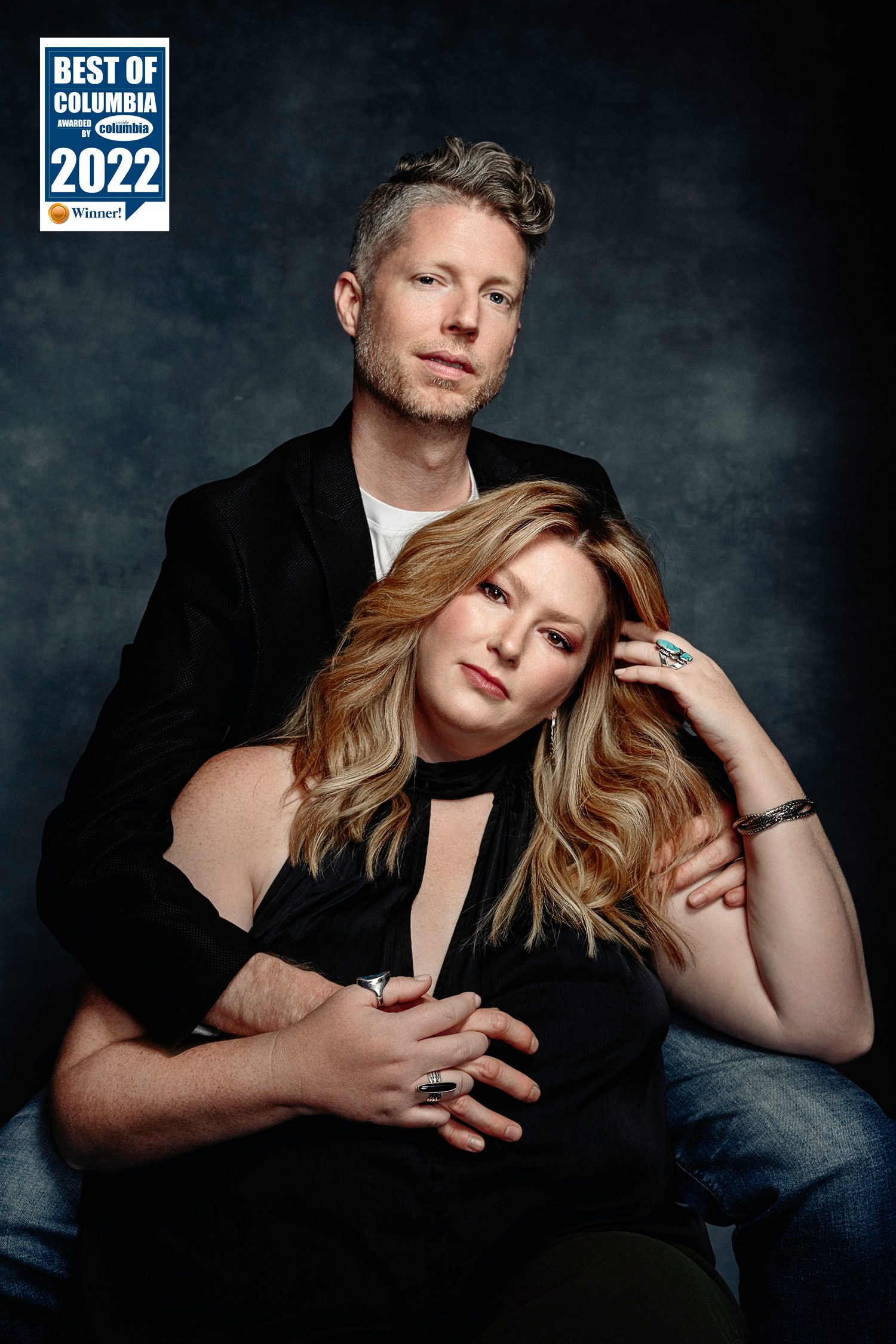 Scott and Shannon Schaefer from Schaefer Photography pose together on blue background after winner best photographer in Columbia as awarded by Inside Columbia Magazine.