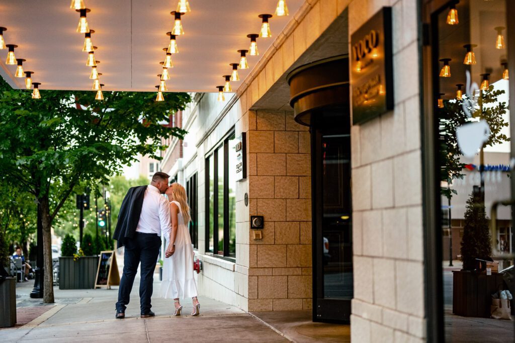 Couple wearing white kiss as they walk on sidewalk in front of Tiger Hotel.