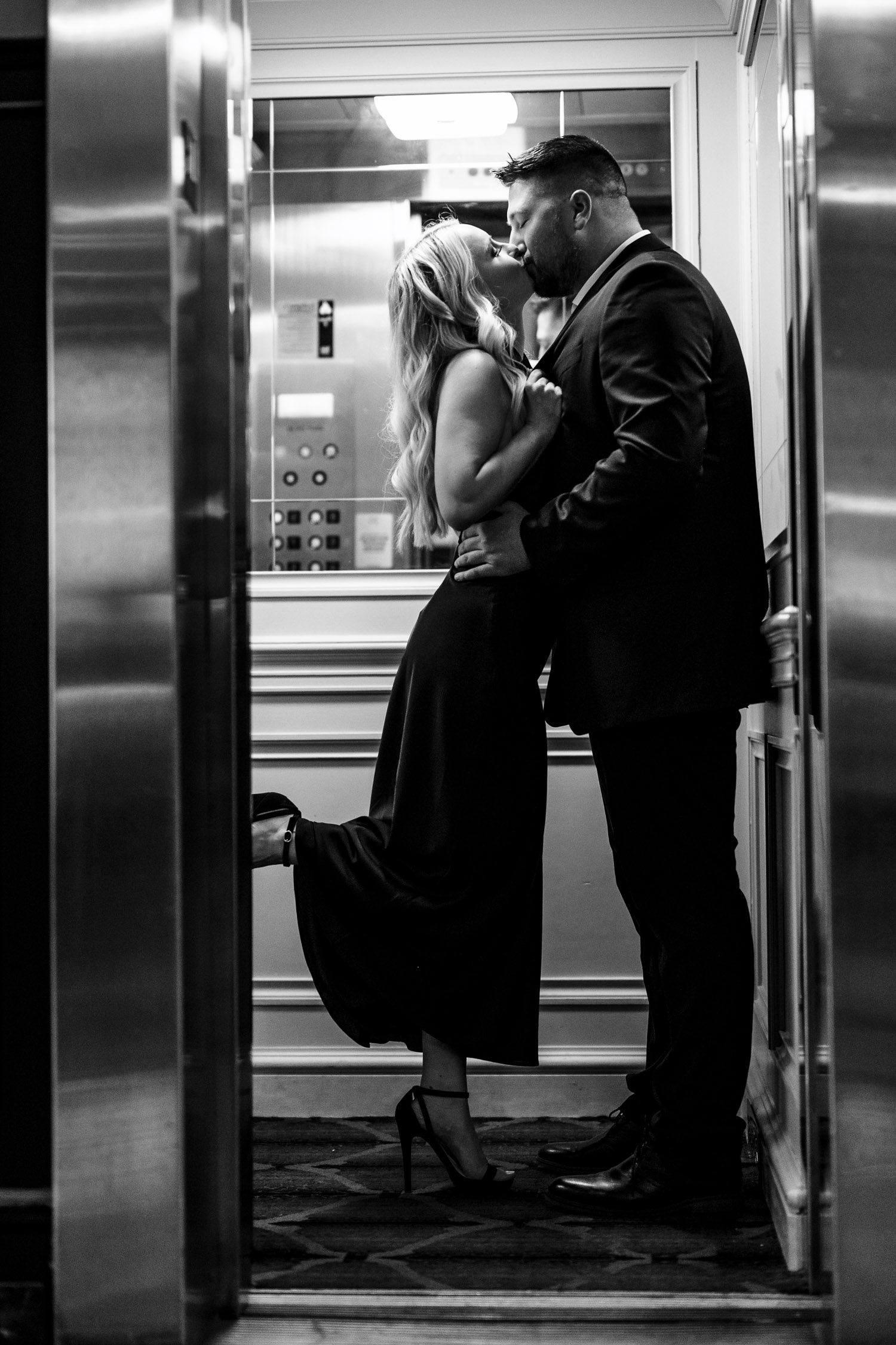 Black and white photo of a blonde girl kissing fiance in Tiger Hotel elevator.

