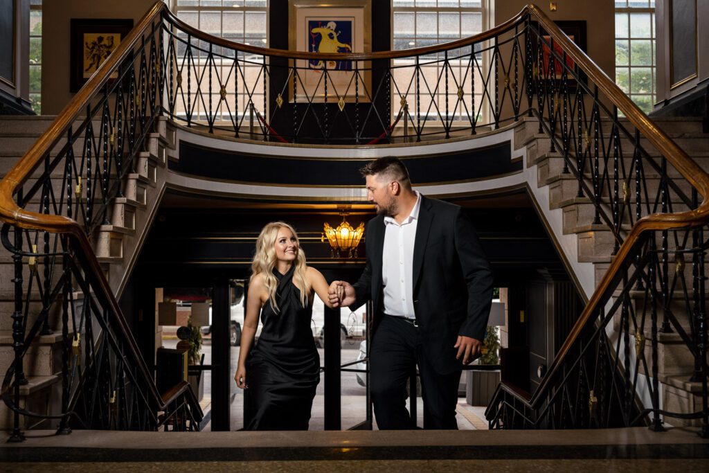 Couple wearing black dress and black suit walk up the Tiger Hotel stairs holding hands.