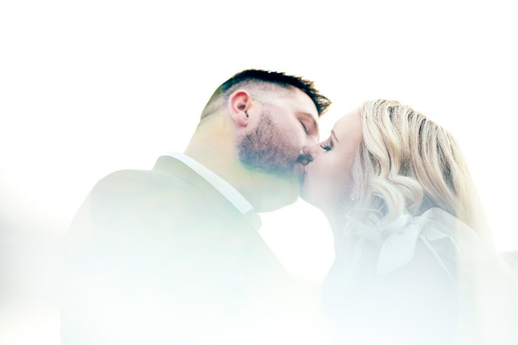 Couple kiss is high key outdoor portrait with sun flare.