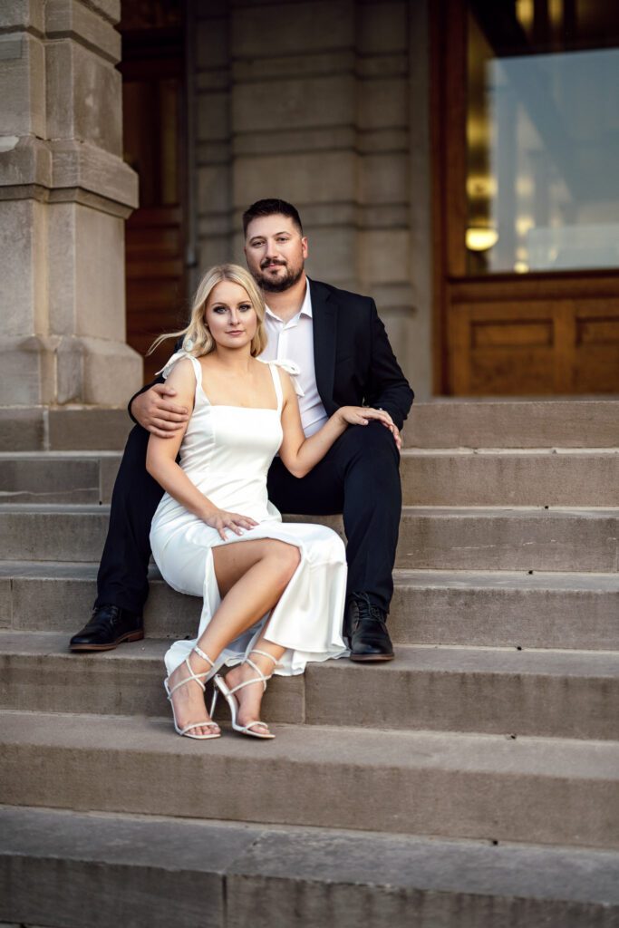 Blonde woman sitting between fiance's legs on steps.