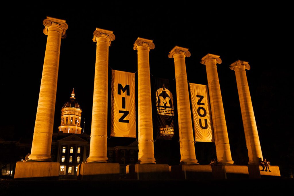 The Mizzou Columns and dome of Jesse Hall are lit up with Yellow Light.