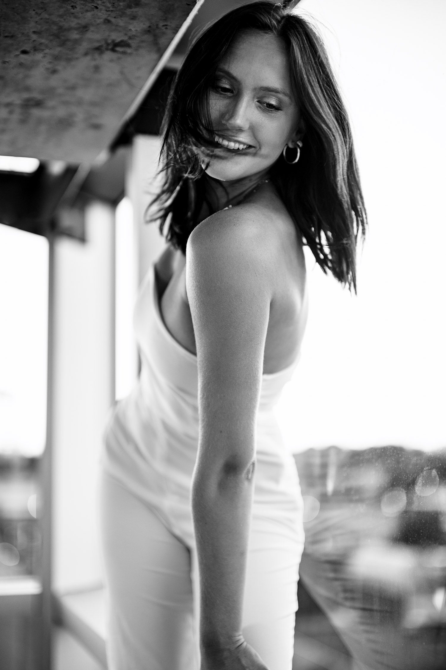 Smiling senior girl smiles with glass windows behind her and her hair flowing.