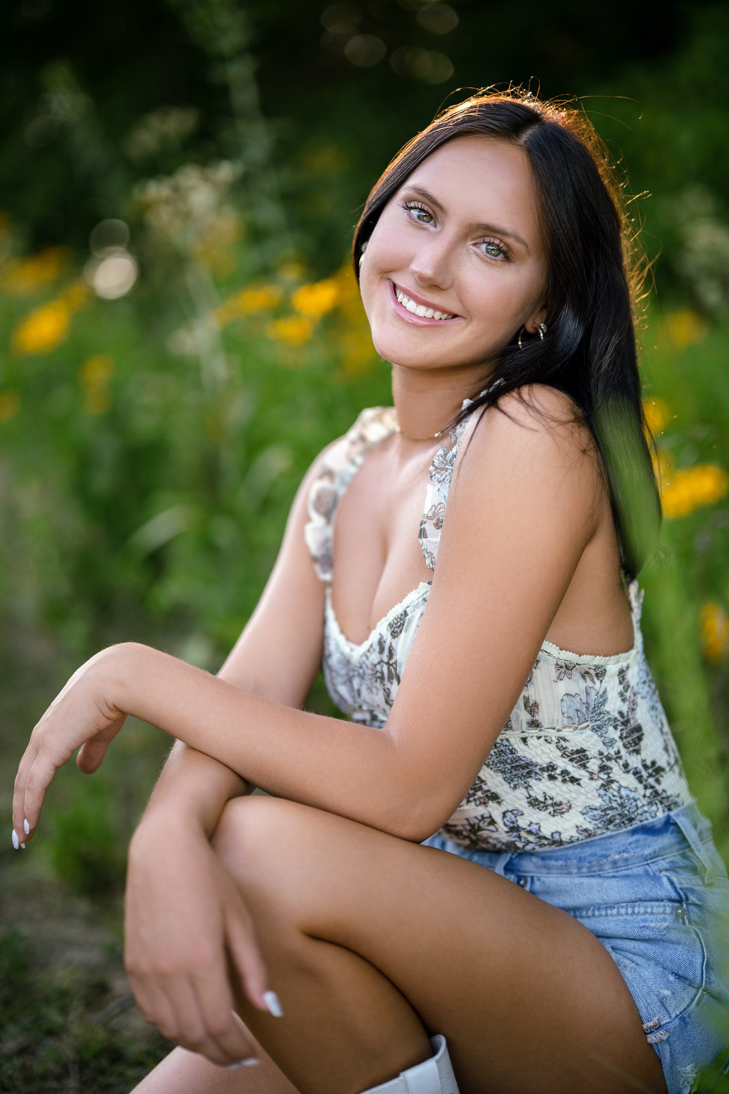 Columbia Missouri senior girl smiling while surrounded by green and yellow flowers.