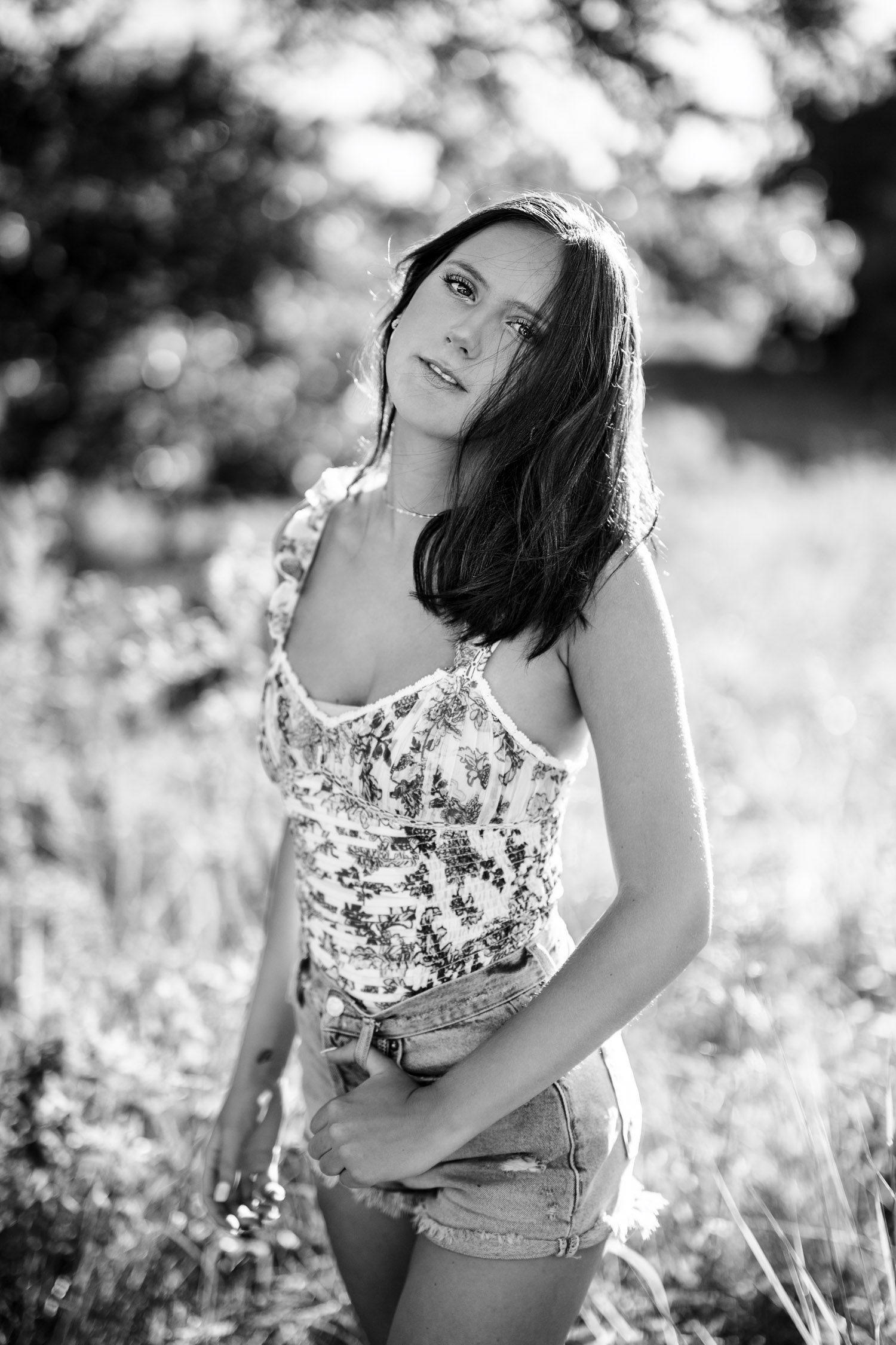 Senior girl with dark hair and wind blown hair in standing in field.