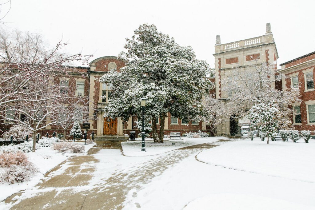 A snowy scene of the Missouri School of Journalism brick buildings including Neff Hall and Walter Williams connected by the Journalism Archway.