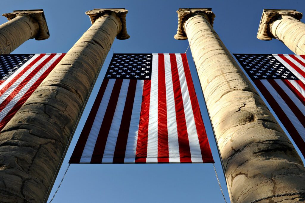 The sun drenched American Flags hang from 4 Concrete Mizzou Columns.