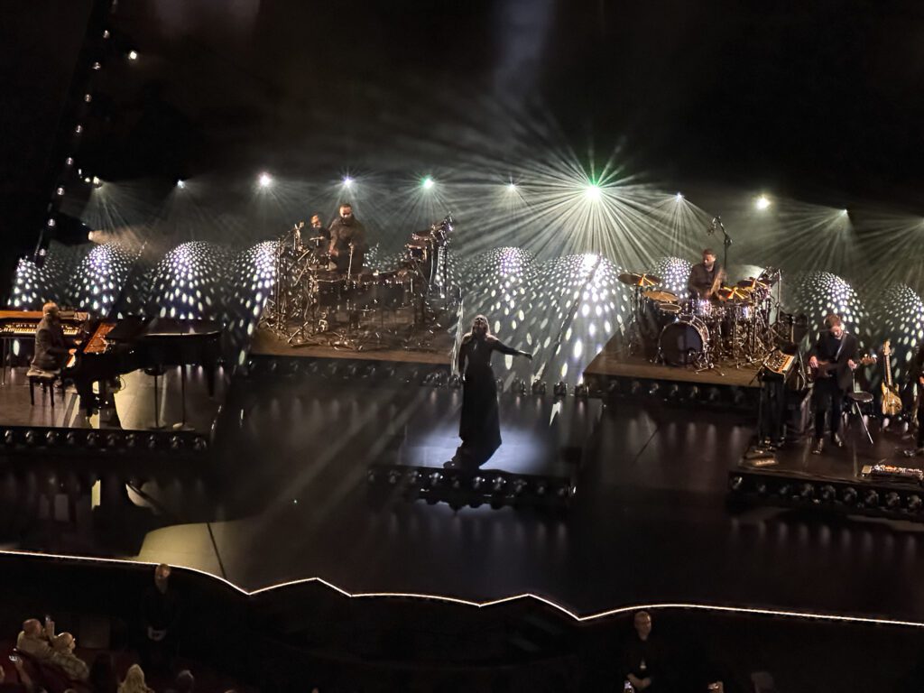 Adele stands in spot light surrounded by band on stage at Caesars Palace Colosseum in Las Vegas.