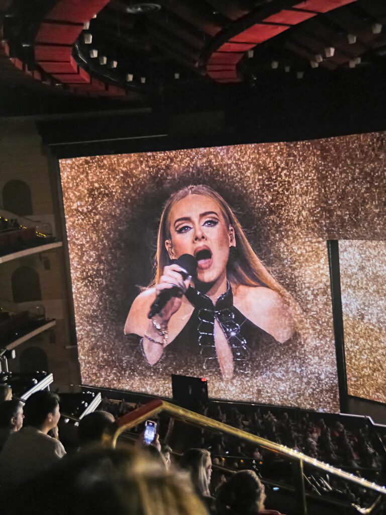 Adele singing into microphone surrounded by gold glitter.