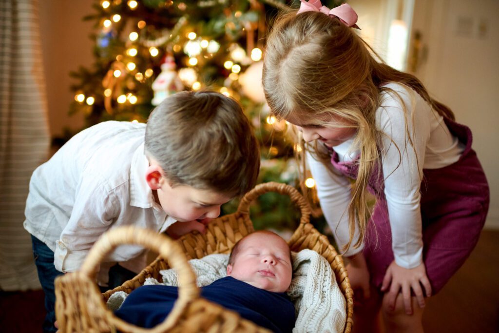 Two children look at newborn baby in basket at Christmas