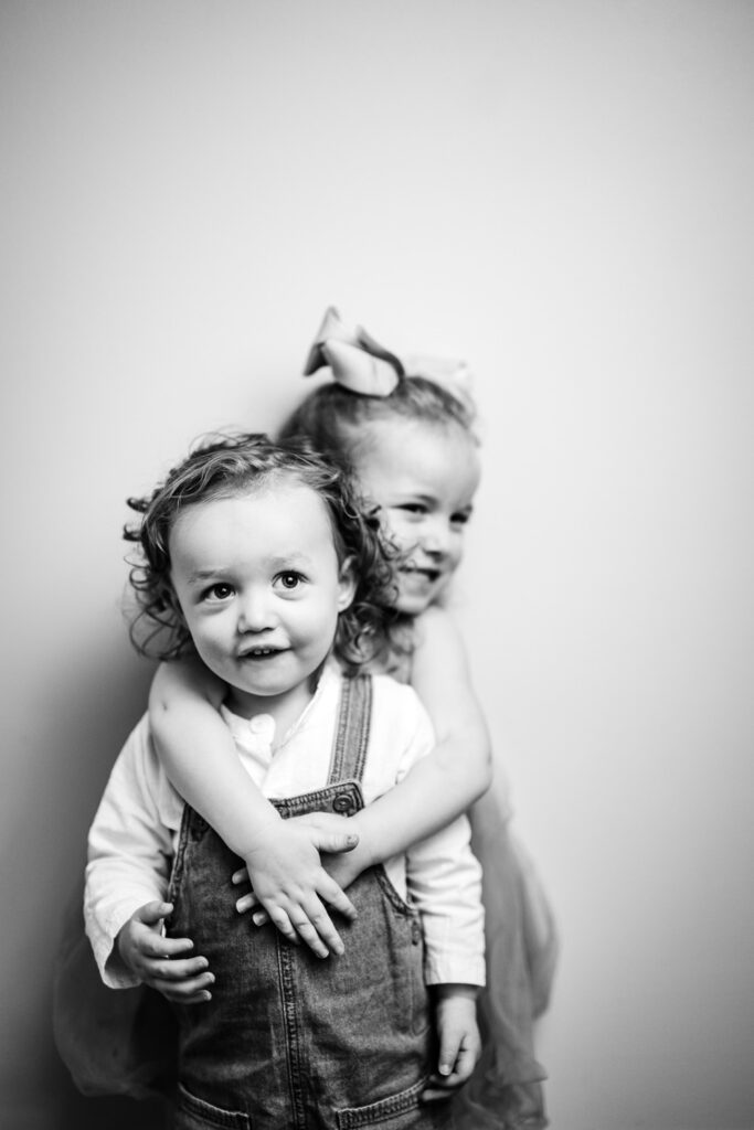 Young girl wearing bow hugs her brother who is wearing overalls.