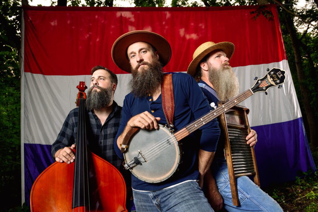 The Kay Brothers pose with banjo, bass and washboard in front of the Missouri State Flag.