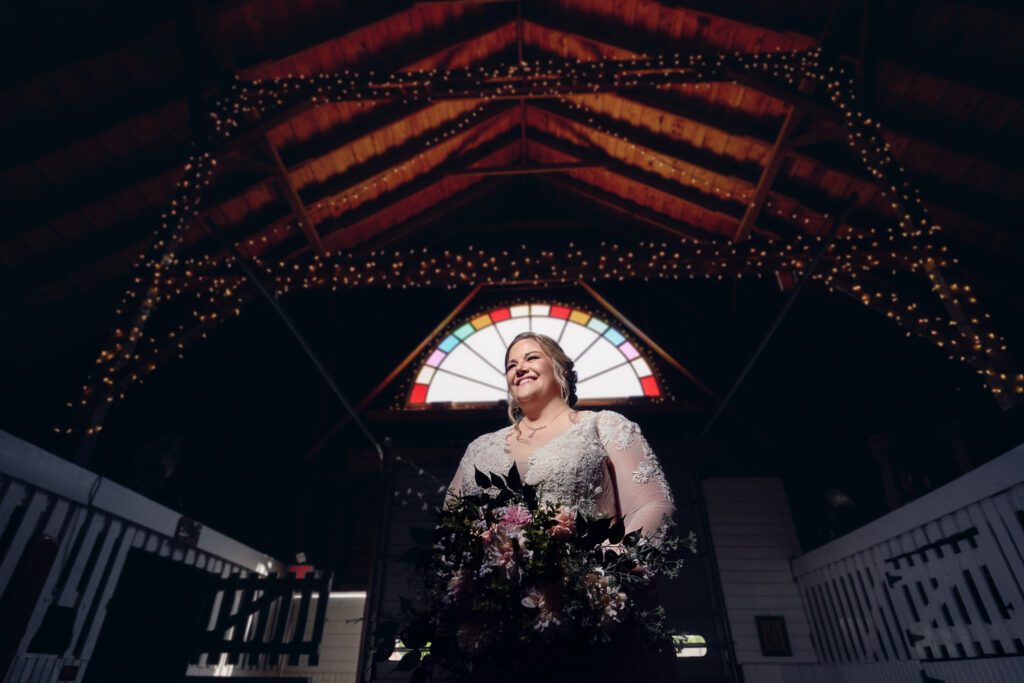 Bride stands in front of stain glass window inside of Simmons Stables in Mexico, Missouri.