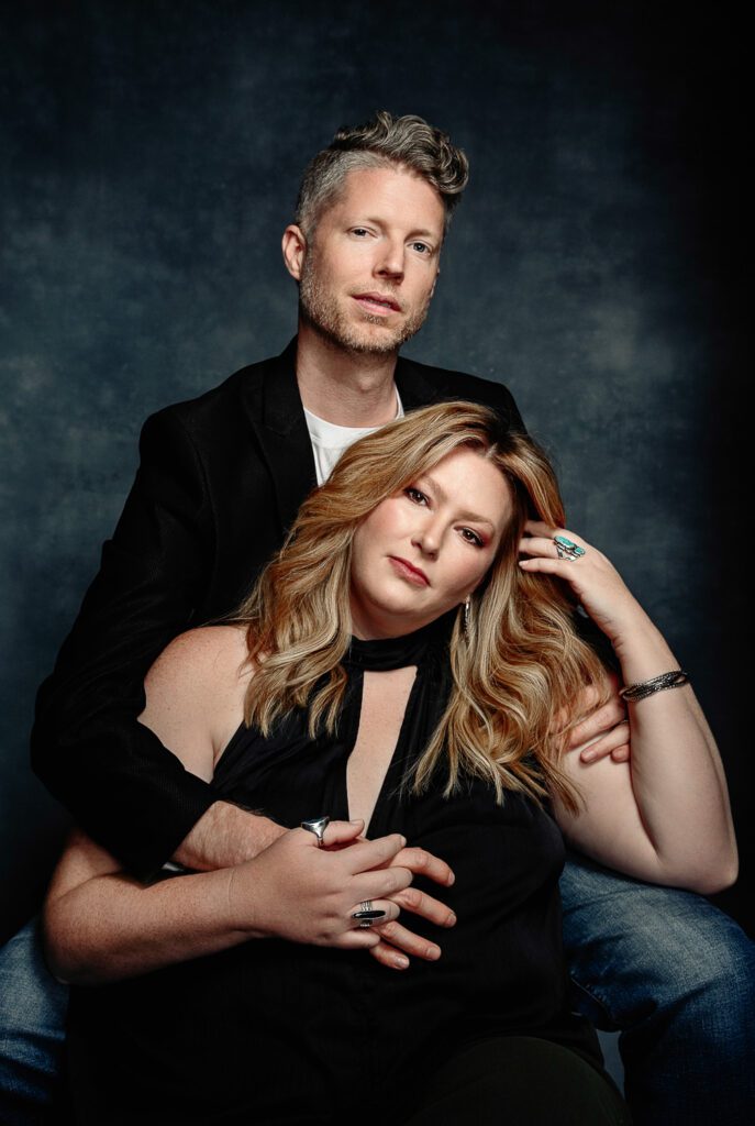 Hot couple pose on blue canvas backdrop wearing turquoise jewelry and black formal wear.